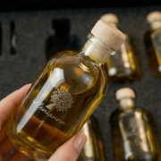 Hand holding an elenianna numbered olive oil sample bottle with a wooden cap inside the luxury tasting kit packaging