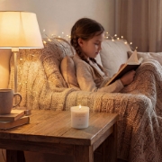 A relaxing indoor scene featuring a lit Aurean Golden Lumos candle on a side table during a cozy evening reading session.